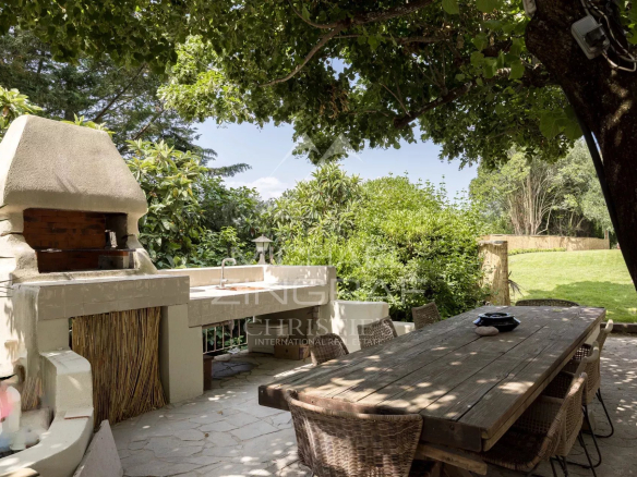 Espace extérieur avec barbecue et table en bois sous des arbres dans une bastide rénovée à Pégomas.