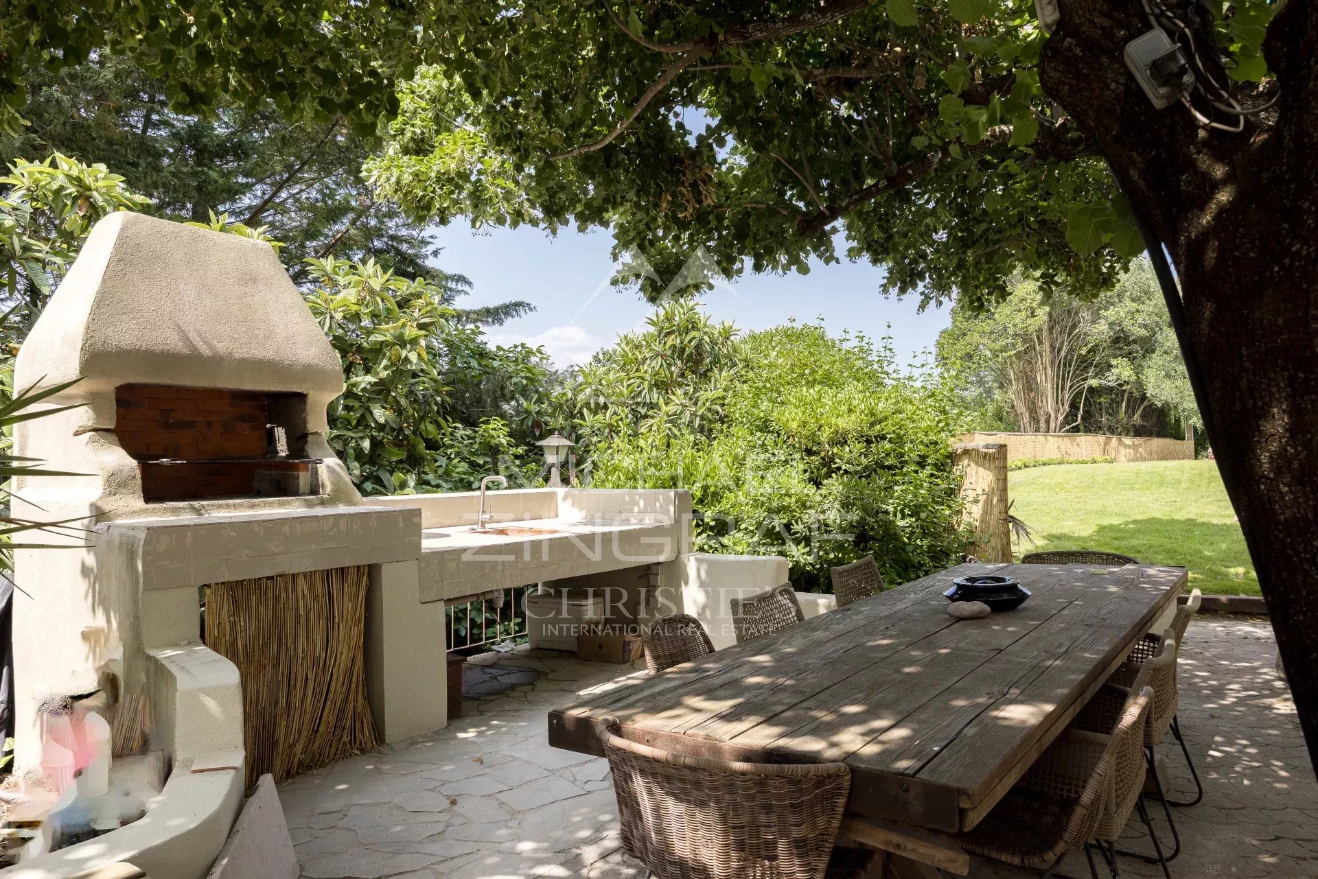 Espace extérieur avec barbecue et table en bois sous des arbres dans une bastide rénovée à Pégomas.