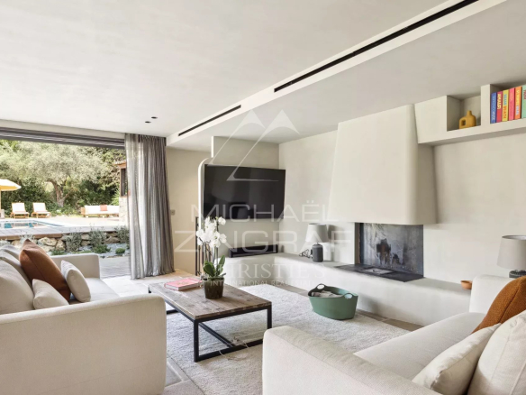 Intérieur d'une bastide rénovée avec salon moderne et cheminée, vue sur la piscine extérieure.