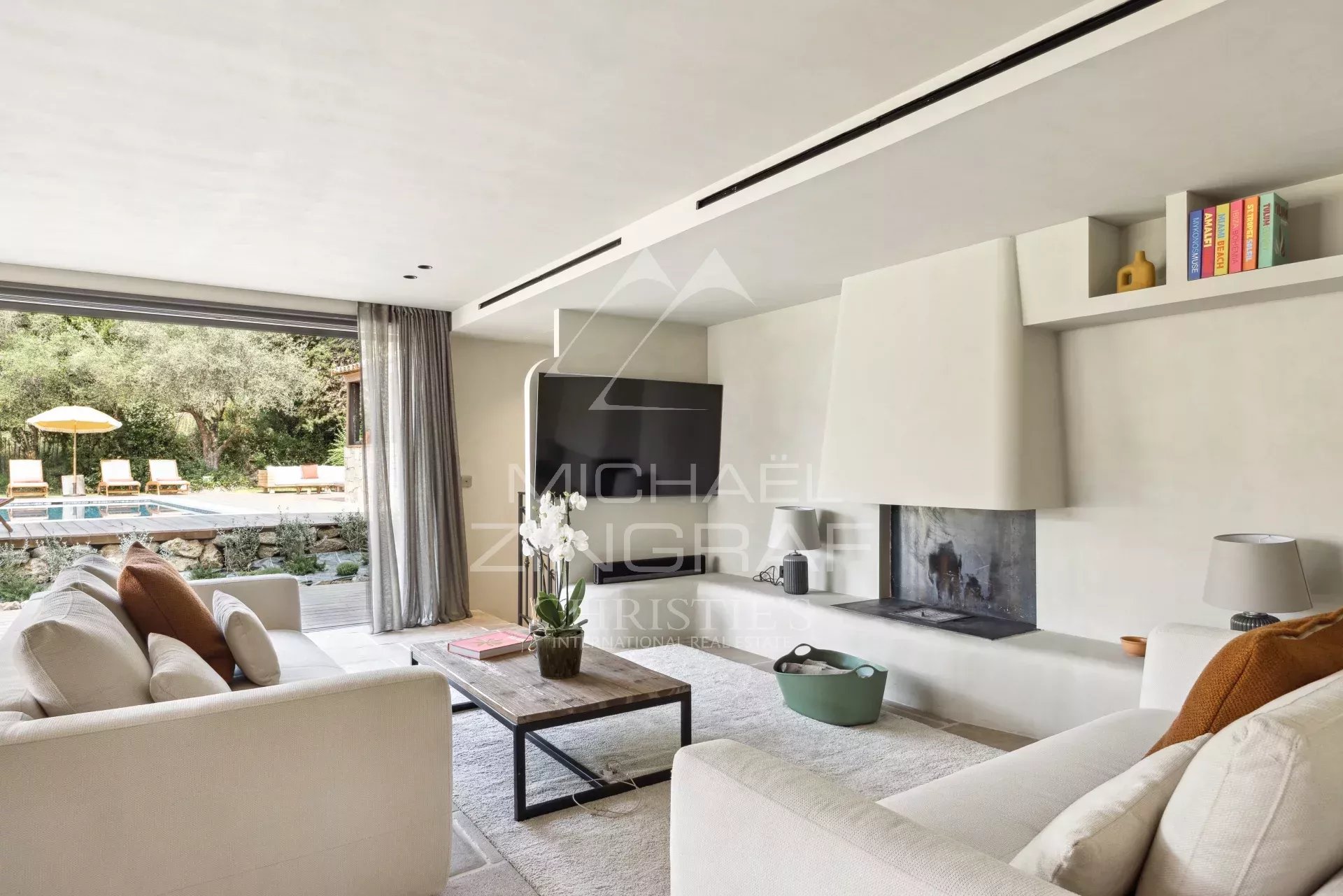 Intérieur d'une bastide rénovée avec salon moderne et cheminée, vue sur la piscine extérieure.