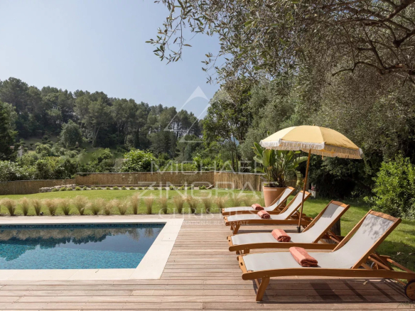 Terrasse avec chaises longues et parasol près d'une piscine, entourée de verdure