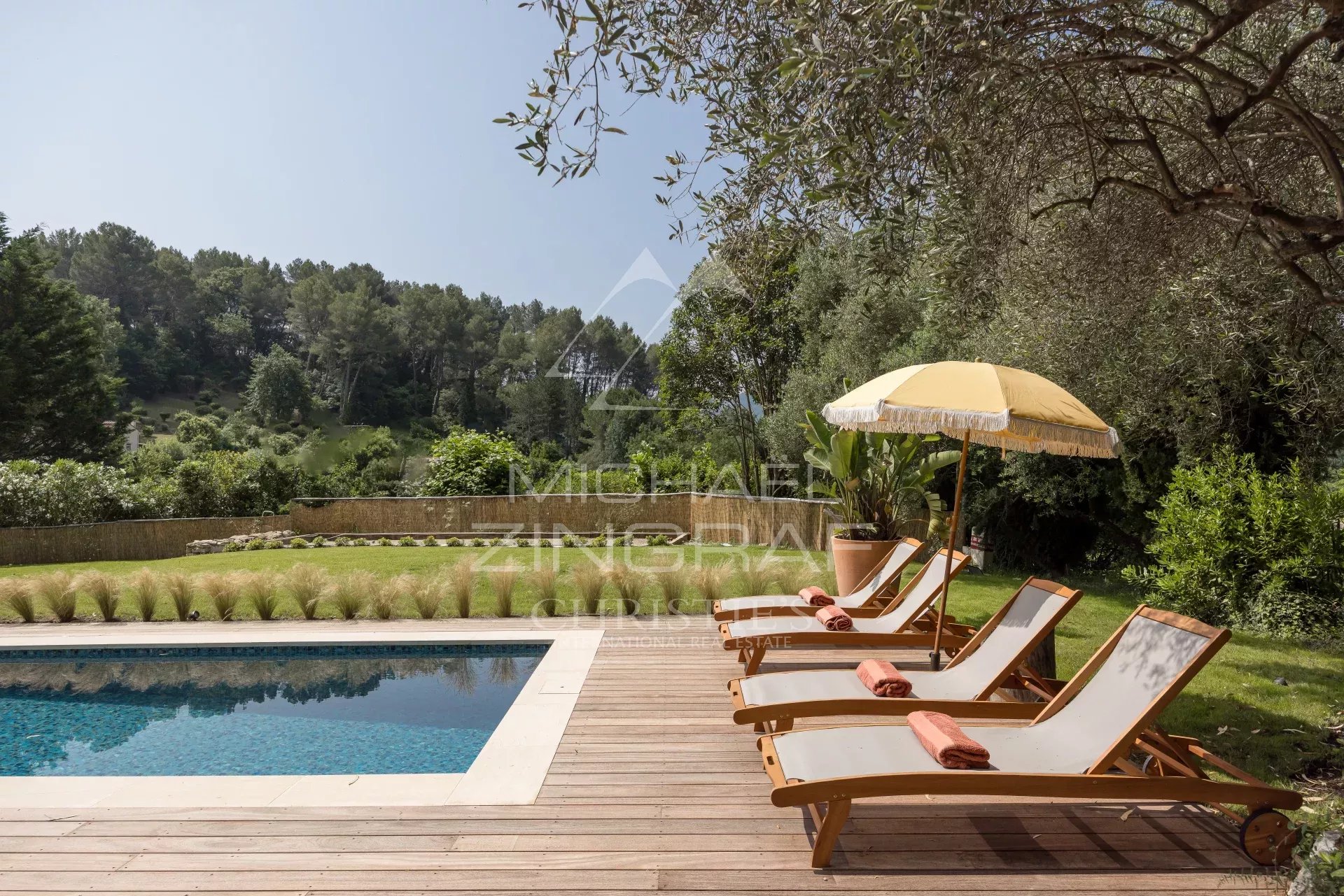 Terrasse avec chaises longues et parasol près d'une piscine, entourée de verdure