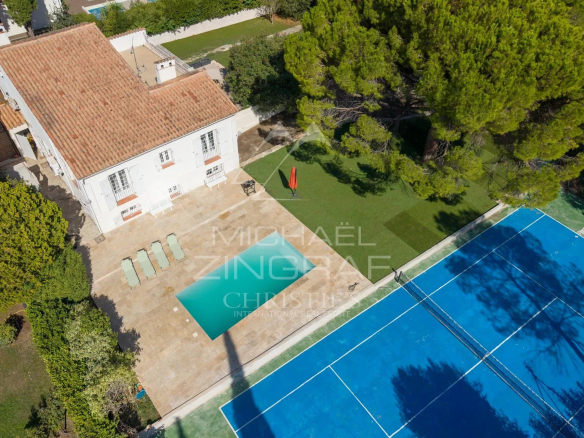 Vue aérienne d'une villa avec piscine et court de tennis à Mougins, entourée d'arbres.