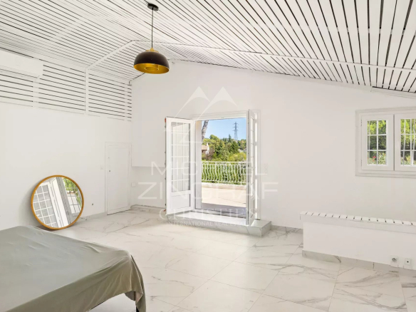 Chambre spacieuse avec fenêtres ouvertes et miroir, dans une villa à Mougins.