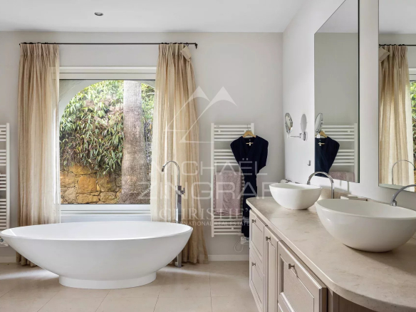 Salle de bain moderne avec baignoire sur pied et double vasque, fenêtres avec vue sur la nature.