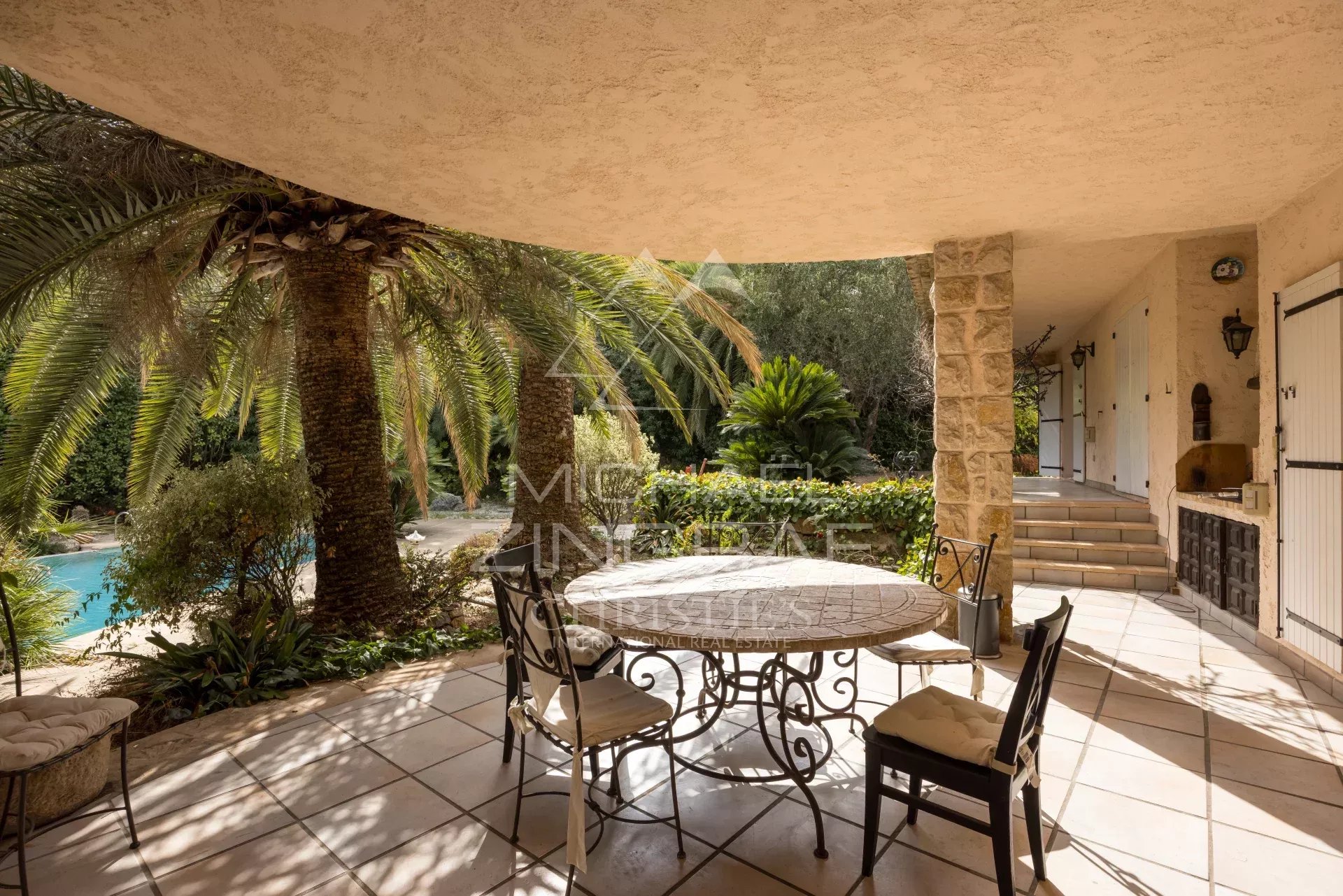 Terrace of a Provençal villa with table and chairs, surrounded by palm trees and greenery in Mougins.