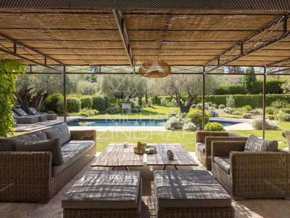 Terrasse couverte avec mobilier en osier, vue sur jardin et piscine dans une villa à Mougins.
