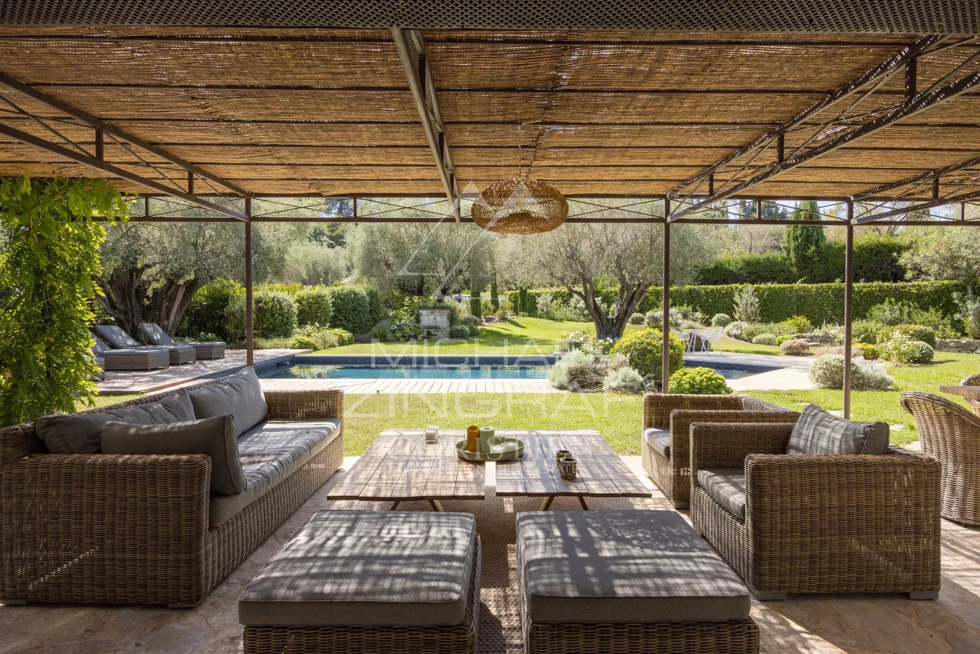 Terrasse couverte avec mobilier en osier, vue sur jardin et piscine dans une villa à Mougins.