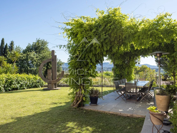 Terrasse d'un mas provençal avec vue sur les collines, entourée de verdure et d'une sculpture moderne.