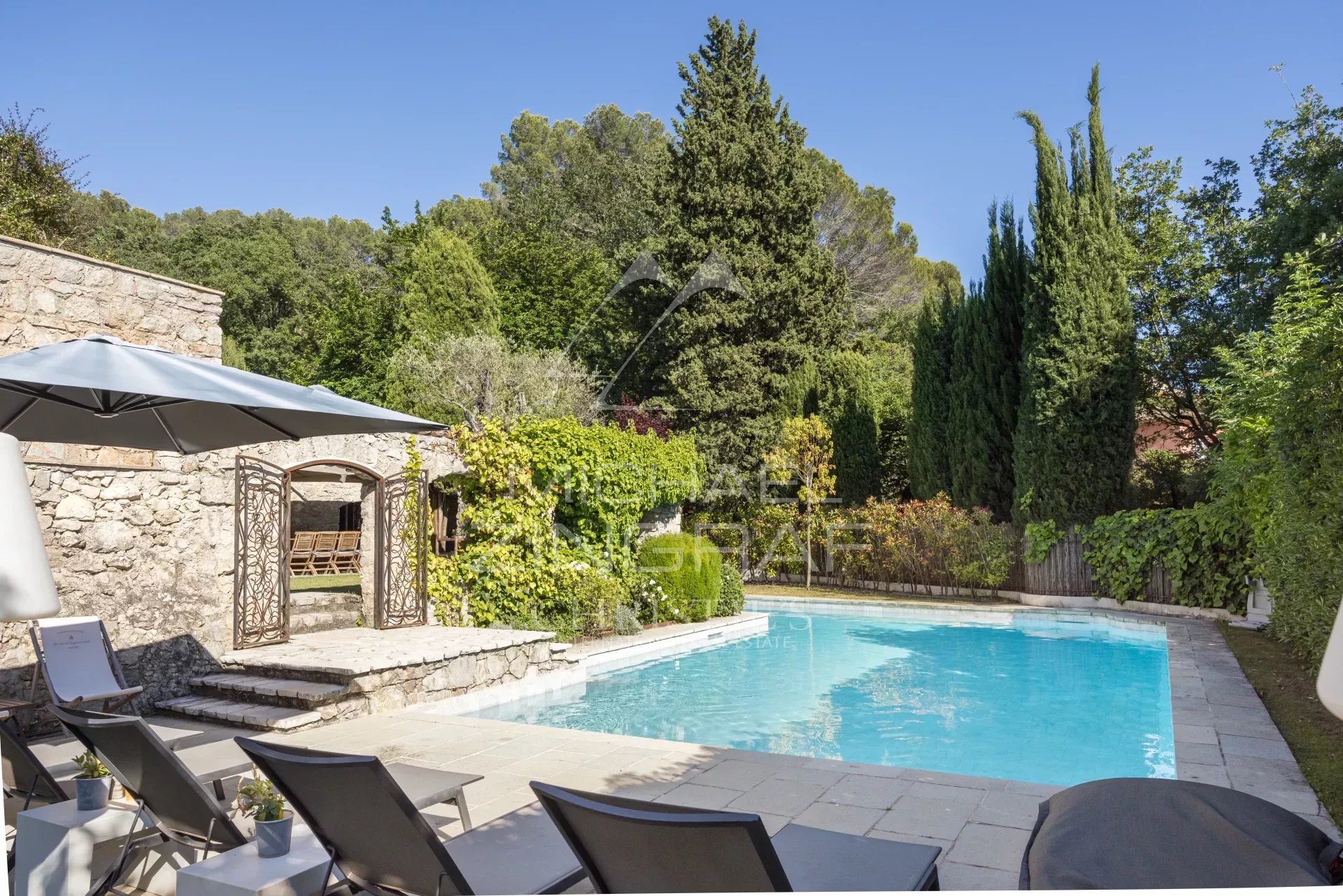 Piscine entourée de verdure et de chaises longues dans un mas provençal rénové.
