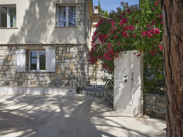 Entrée d'une villa en pierre avec des fleurs et un portail, située à Mougins.