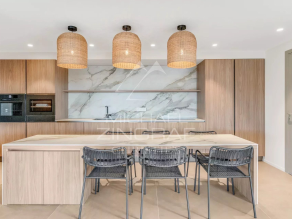 Modern kitchen with a marble backsplash, wooden cabinets, and a light-colored island; three woven pendant lights above and black wire chairs along the island.