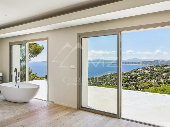 Modern bathroom with a white freestanding tub beside large sliding glass doors revealing a coastal landscape. Tip: concisely describes the scene and purpose (bathroom with view).