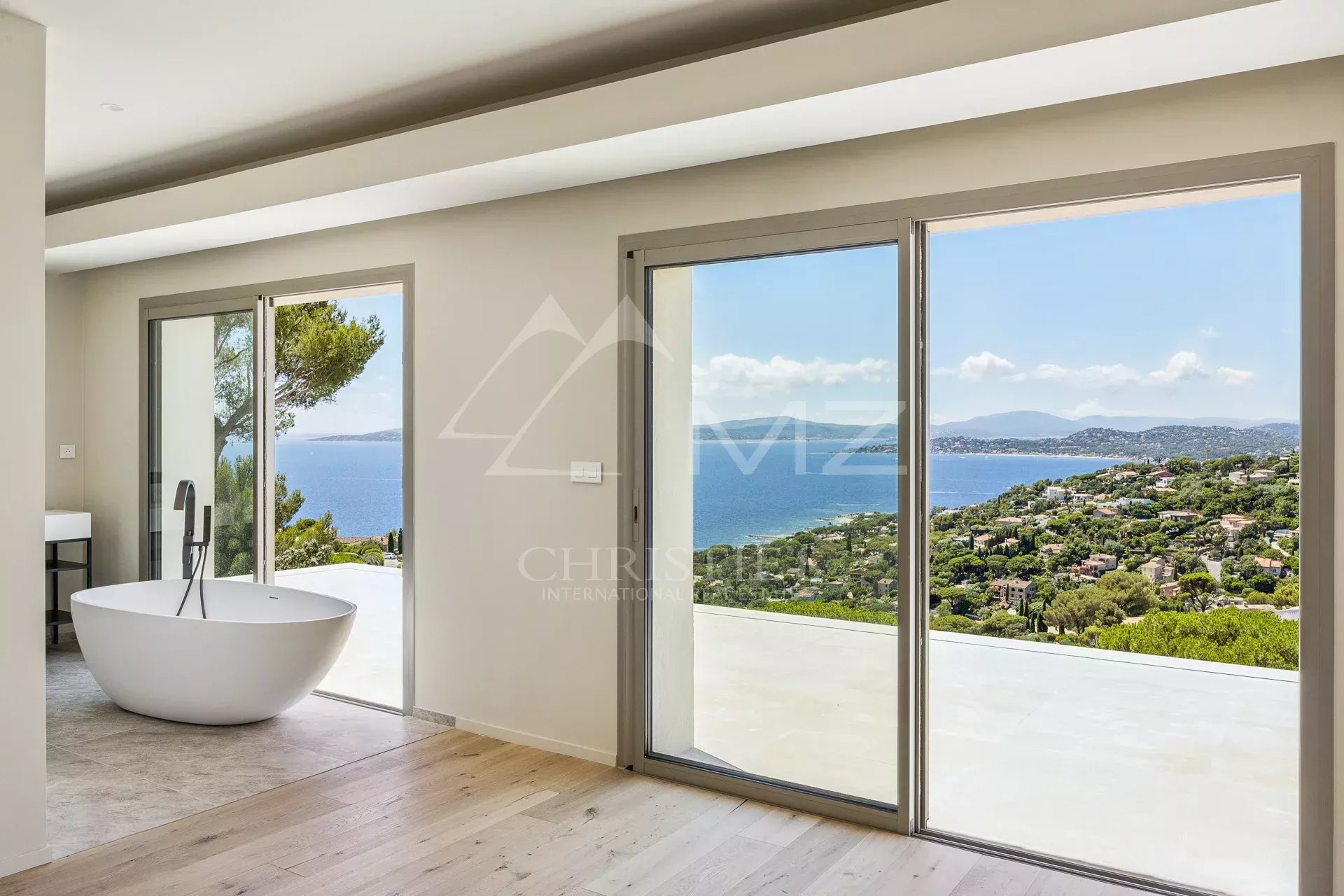 Modern bathroom with a white freestanding tub beside large sliding glass doors revealing a coastal landscape. Tip: concisely describes the scene and purpose (bathroom with view).
