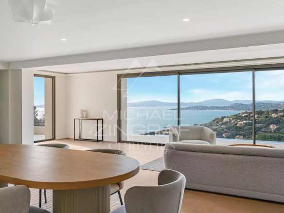 Spacious living area with a round wooden dining table and gray chairs, and large windows offering a coastal panorama.