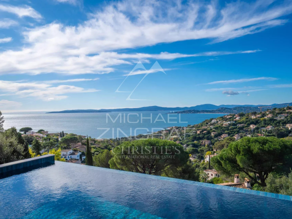 Infinity pool in the foreground with a coastal town, sea, and blue sky beyond.