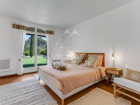 Bright bedroom with peach bedding, white furniture, and a large French door opening to a green garden.