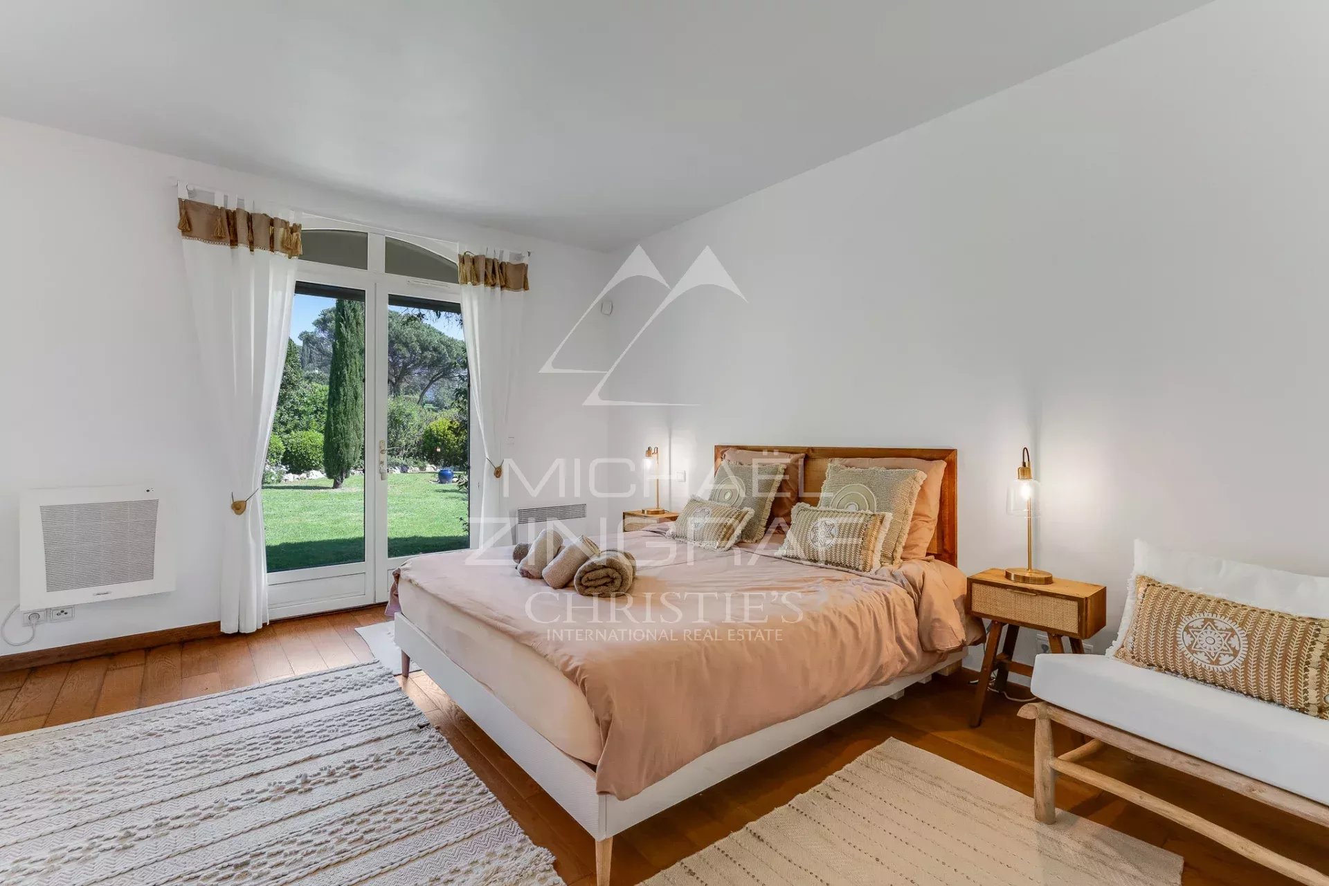 Bright bedroom with peach bedding, white furniture, and a large French door opening to a green garden.