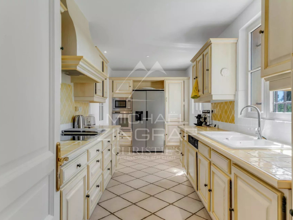 Bright cream kitchen with gold-trim cabinets, yellow tile backsplash, and stainless appliances along a narrow galley.