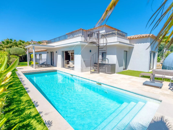 Modern white villa with a rectangular blue pool, spiral staircase, and outdoor lounge on a sunny day.