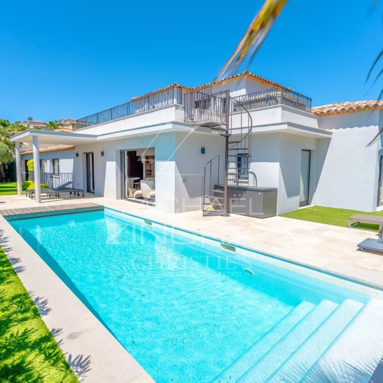 Modern white villa with a rectangular blue pool, spiral staircase, and outdoor lounge on a sunny day.