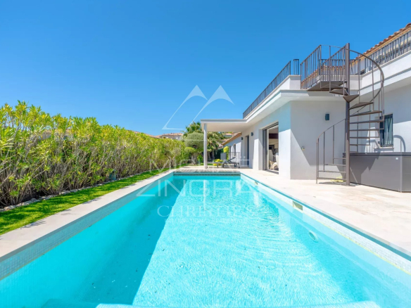 Modern white villa with a long rectangular pool, spiral metal staircase, and clear blue sky.