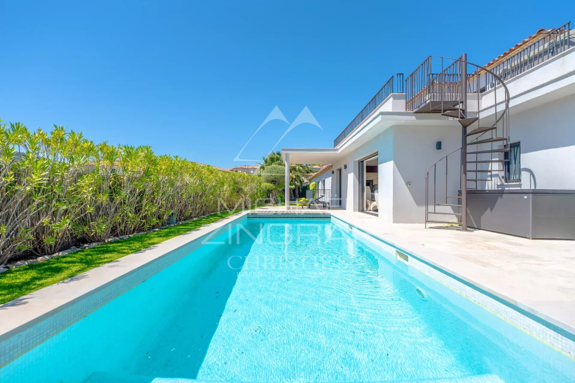 Modern white villa with a long rectangular pool, spiral metal staircase, and clear blue sky.