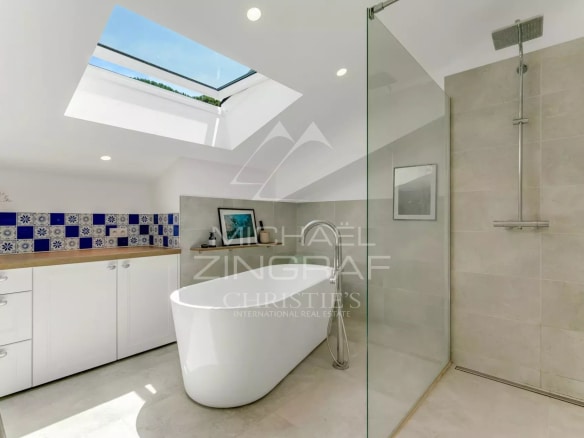 Salle de bain moderne avec baignoire et douche, carrelage beige et murs décorés de carreaux bleus.