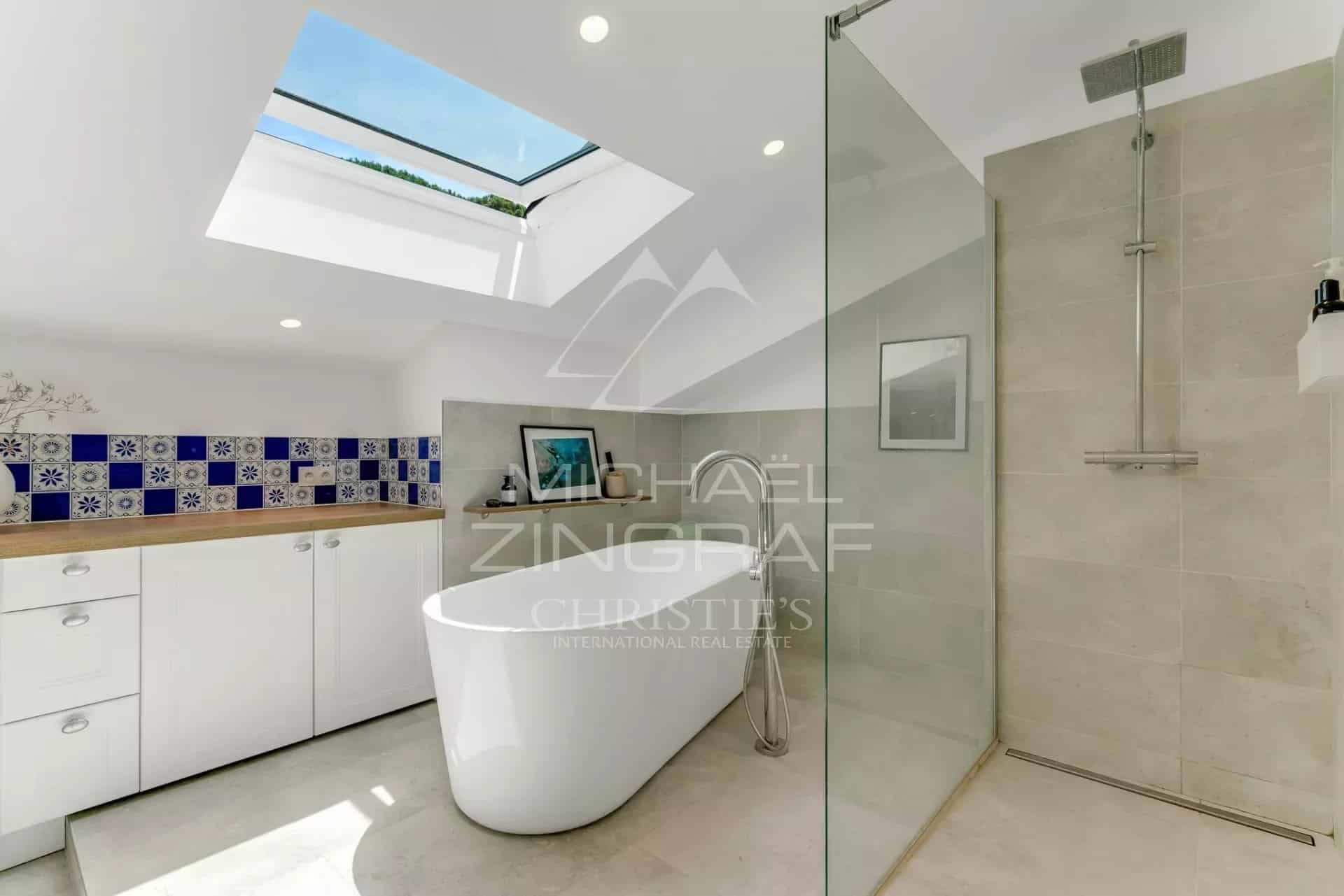 Salle de bain d’un appartement à Sainte-Maxime Salle de bain moderne avec baignoire et douche, carrelage beige et murs décorés de carreaux bleus.