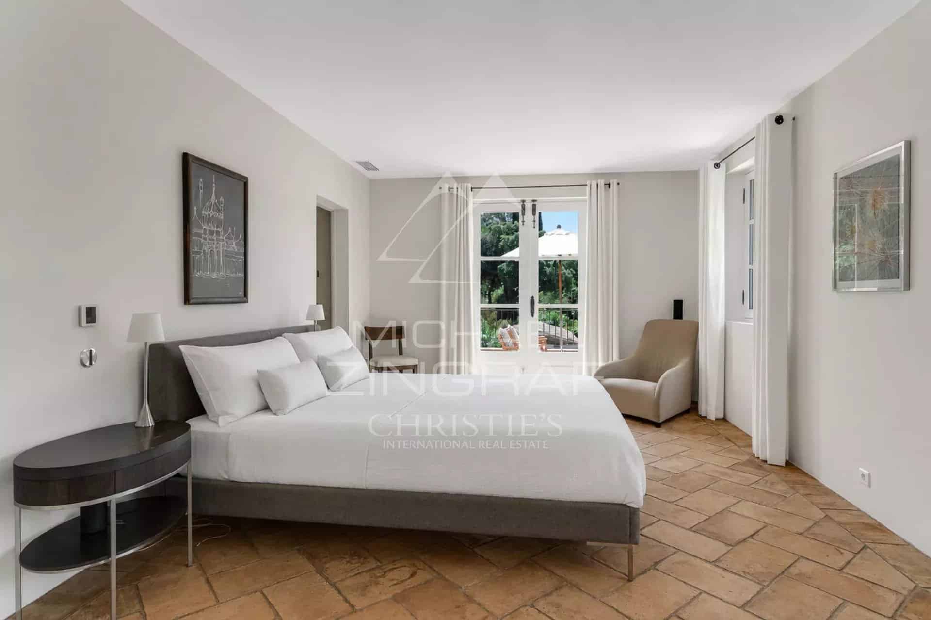 Chambre d'une villa provençale à Ramatuelle, avec un lit double et des fenêtres donnant sur le jardin.