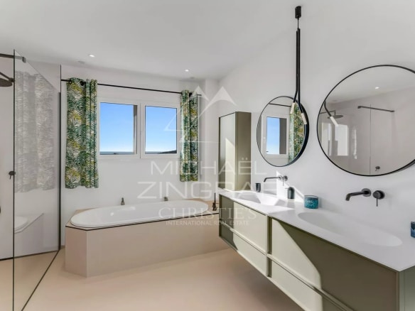 Salle de bain moderne avec baignoire et douche, fenêtres offrant une vue sur la mer.