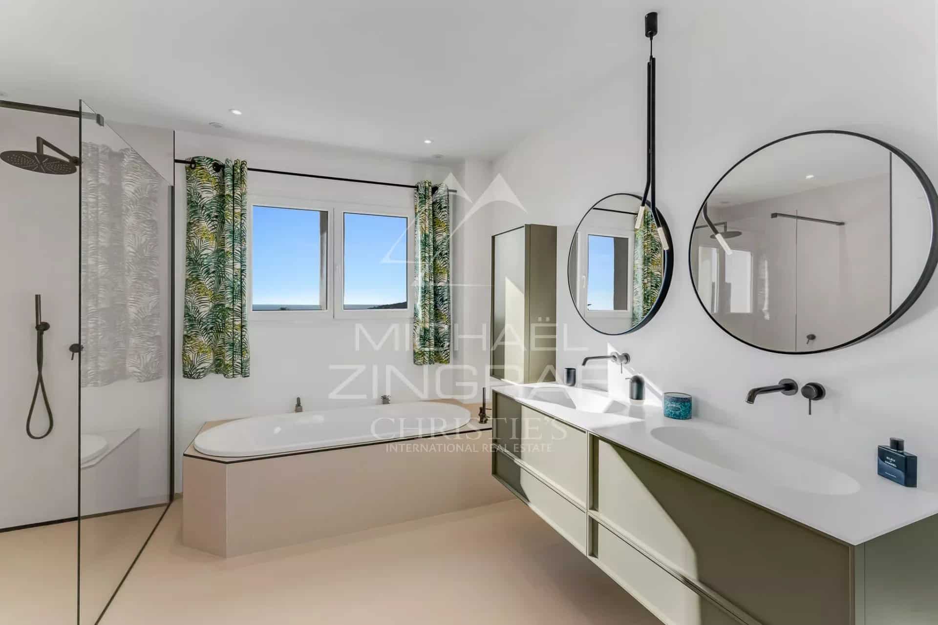 Salle de bain moderne avec baignoire et douche, fenêtres offrant une vue sur la mer.