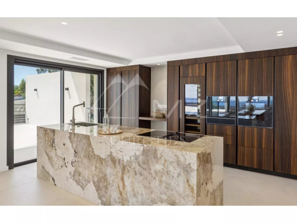 Modern kitchen with a stone island and wooden storage, sea view.