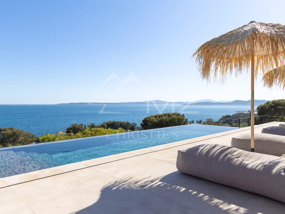 Vue sur la mer depuis une villa contemporaine avec piscine à débordement et transats.