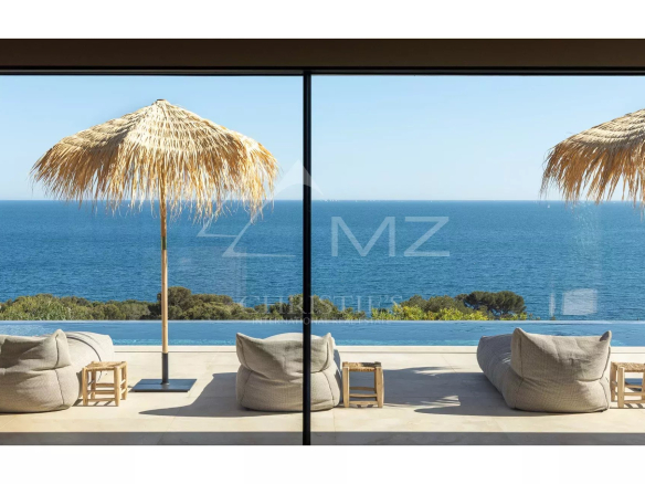 Vue sur la mer depuis une villa contemporaine avec parasols et transats.