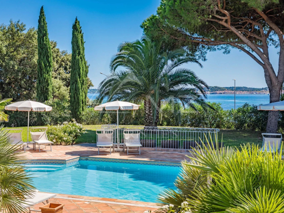 Vue d'une piscine entourée de verdure et de palmiers, avec la mer en arrière-plan à Grimaud.