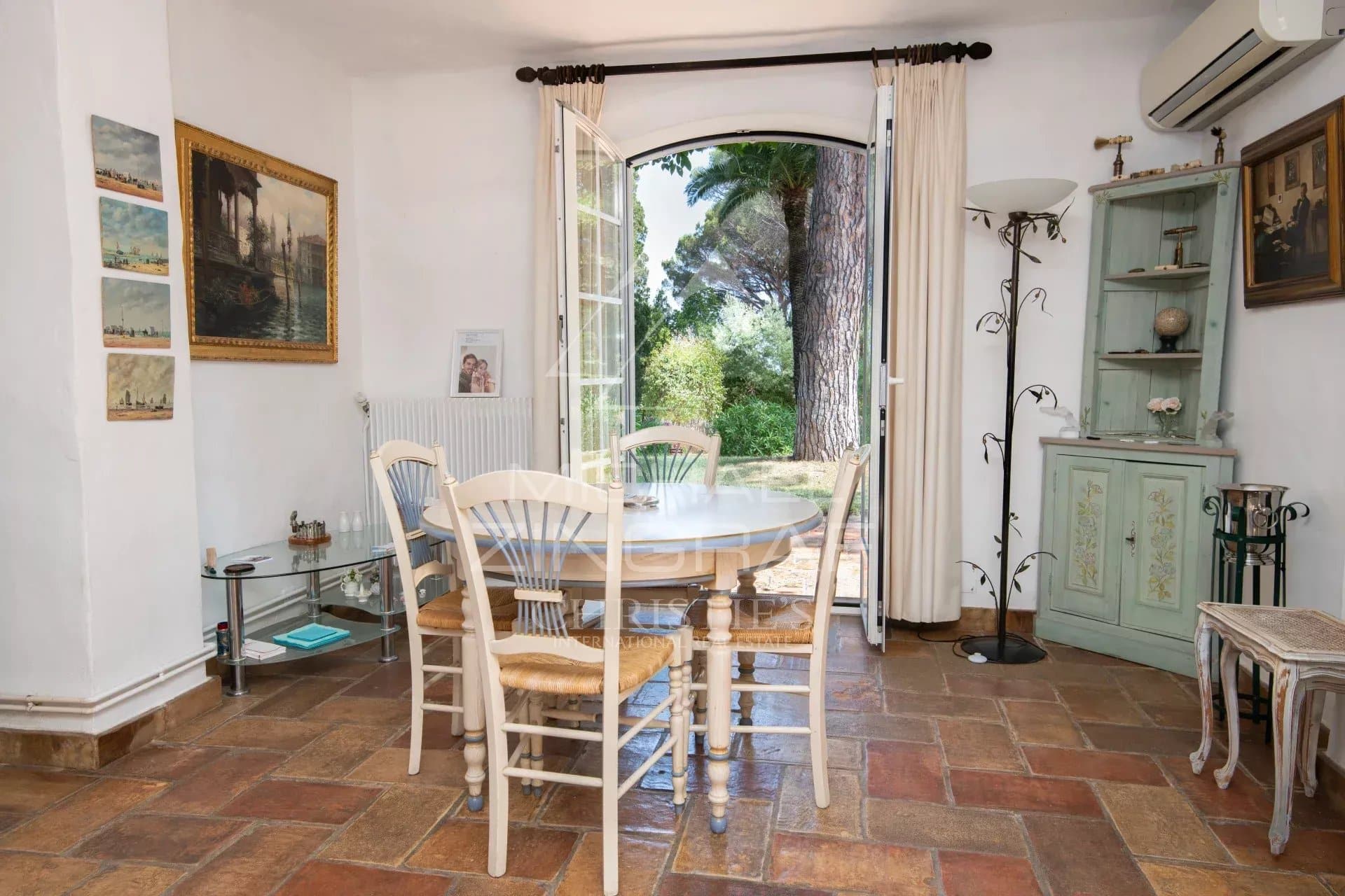 Salle à manger de la villa à Sainte-Maxime Salle à manger lumineuse avec vue sur le jardin, décorée de meubles en bois et d'œuvres d'art.