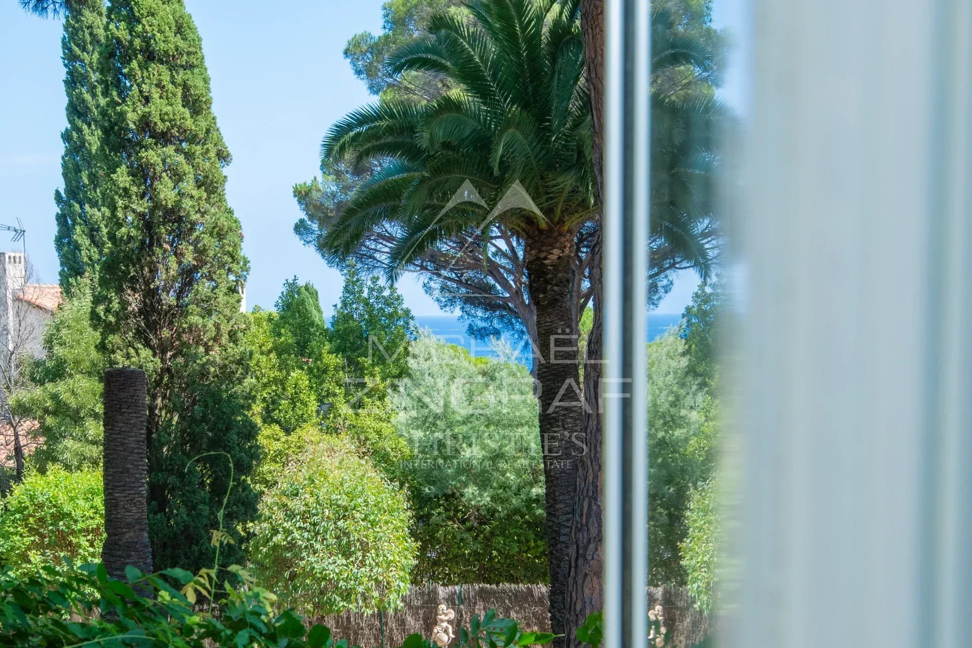 Propriété d’exception à Sainte-Maxime Vue sur un jardin paysager avec des palmiers et des arbres, à proximité de la mer.