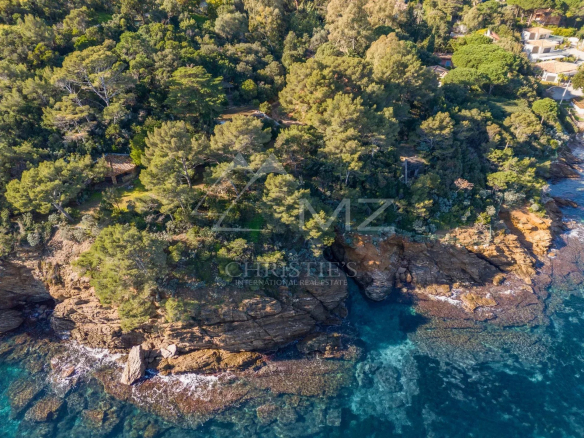 Vue aérienne d'une propriété côtière au Lavandou, entourée de verdure et de rochers au bord de la mer.