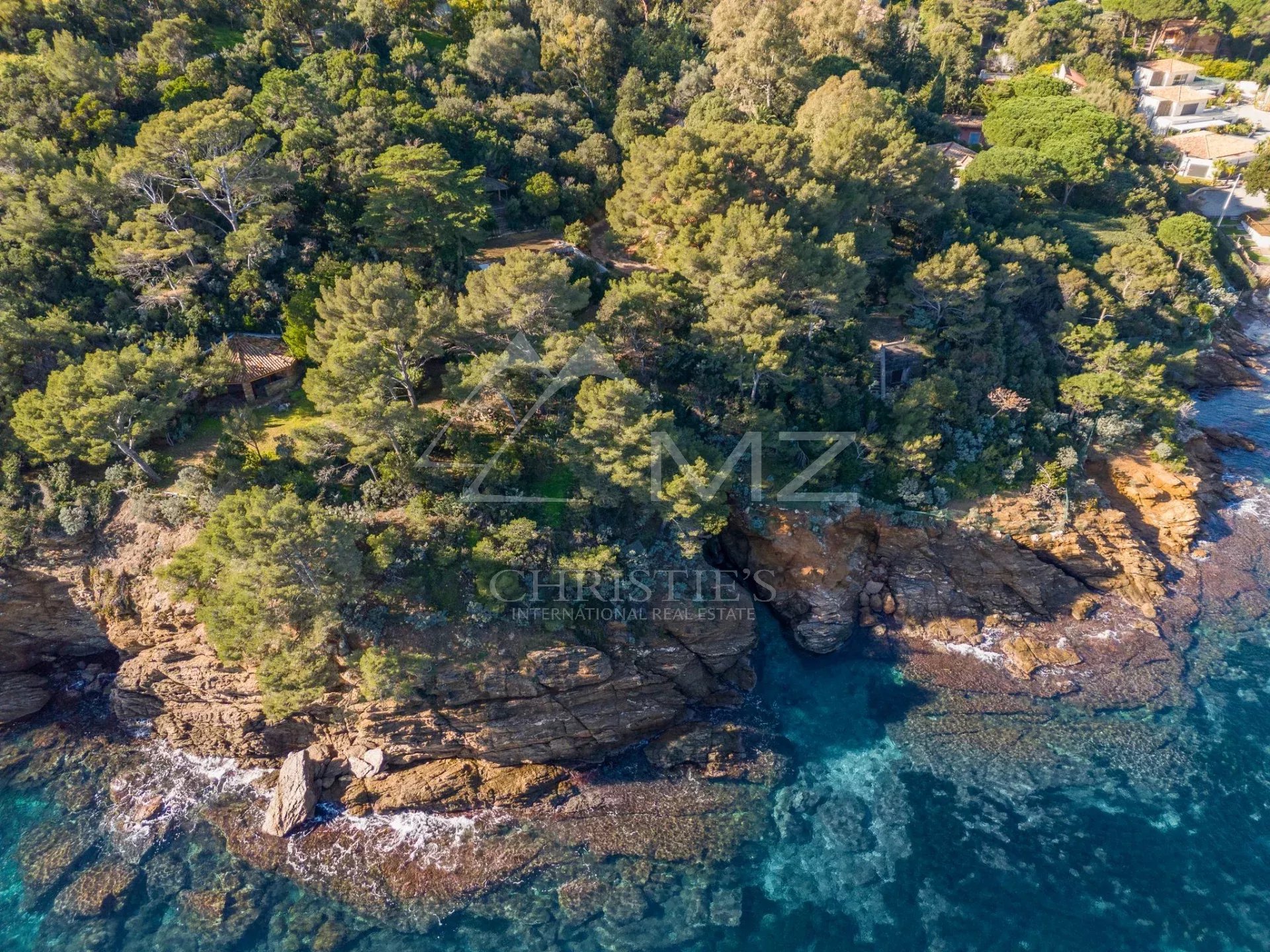 Vue aérienne d'une propriété côtière au Lavandou, entourée de verdure et de rochers au bord de la mer.
