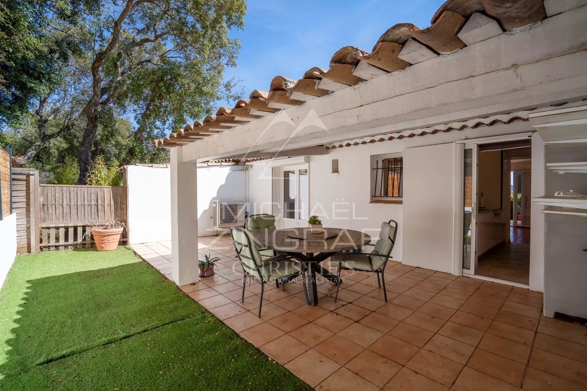 Terrasse d'une maison avec mobilier de jardin, vue sur un espace vert.