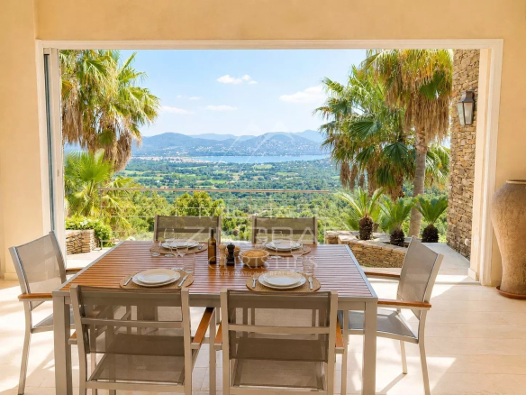 Terrace of a modern villa with views of the sea and mountains, surrounded by palm trees.