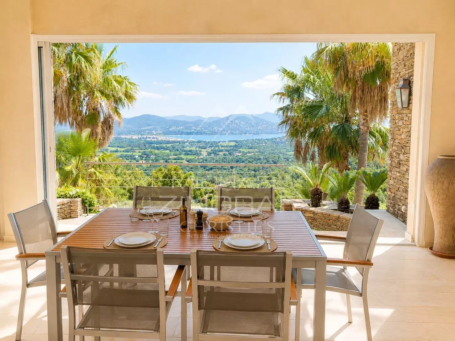 Exceptional villa in Saint-Tropez Terrace of a modern villa with views of the sea and mountains, surrounded by palm trees.