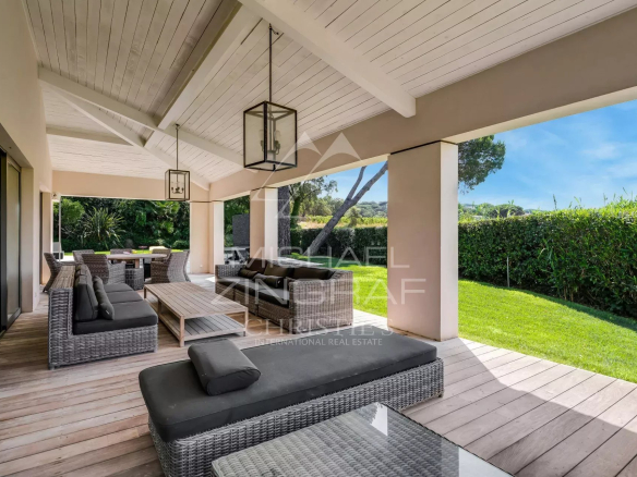 Terrasse d'une maison spacieuse avec mobilier en osier et vue sur un jardin verdoyant.