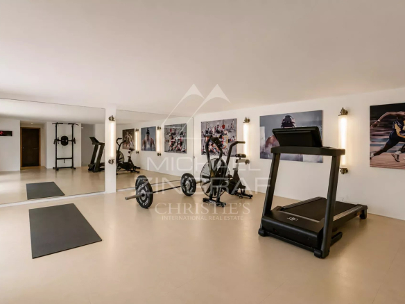 Salle de sport équipée avec tapis de course et poids, murs décorés de photos de sportifs.