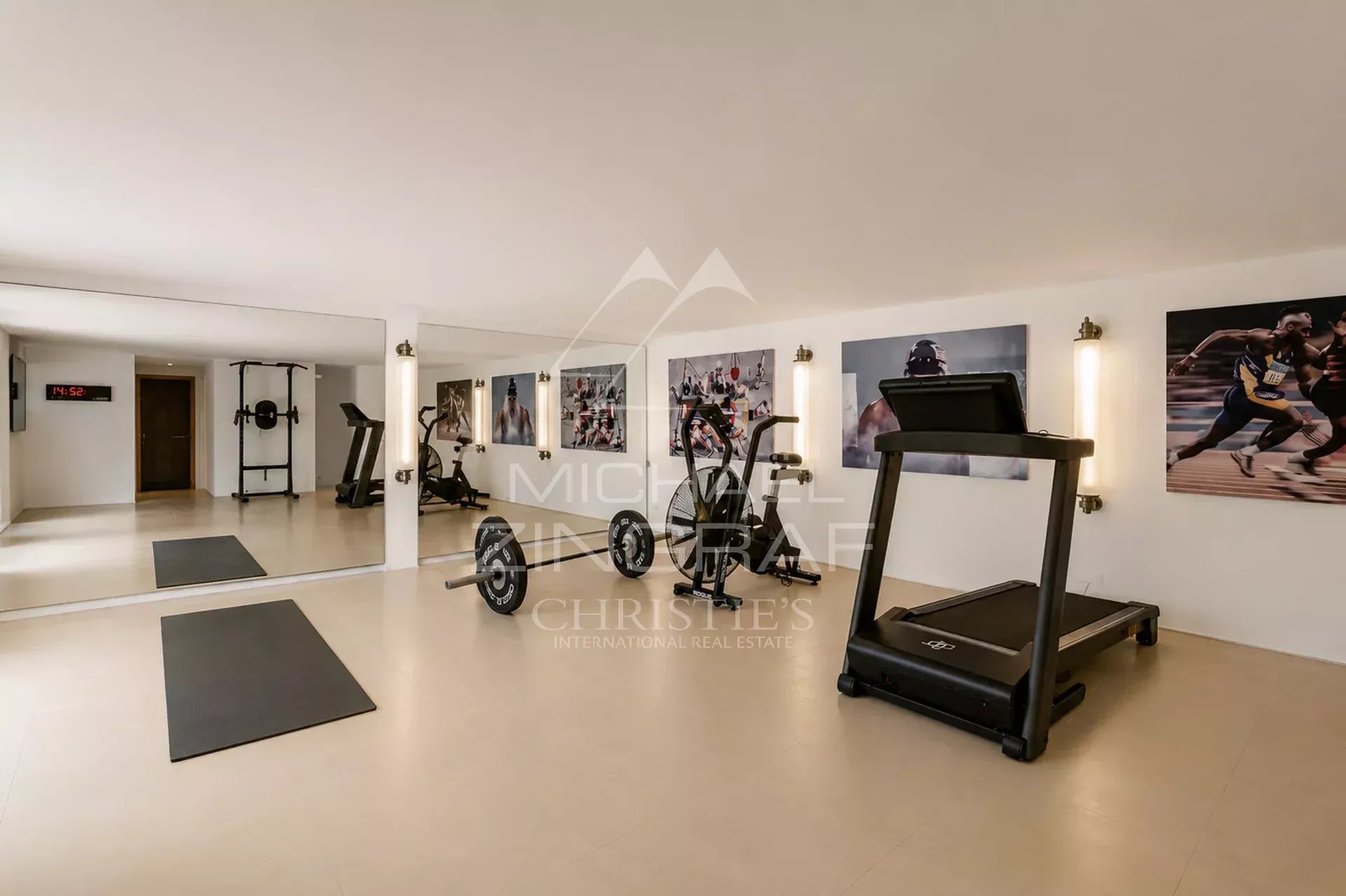 Salle de sport à Saint-Tropez Salle de sport équipée avec tapis de course et poids, murs décorés de photos de sportifs.