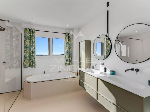 Salle de bain moderne avec baignoire et douche, fenêtres offrant une vue sur la mer.