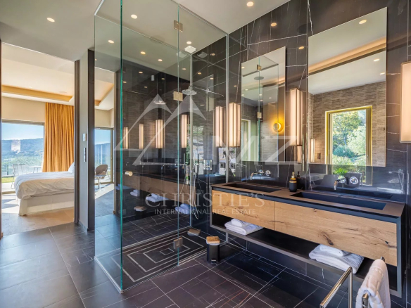 Salle de bain moderne avec douche en verre et double vasque, vue sur la nature.