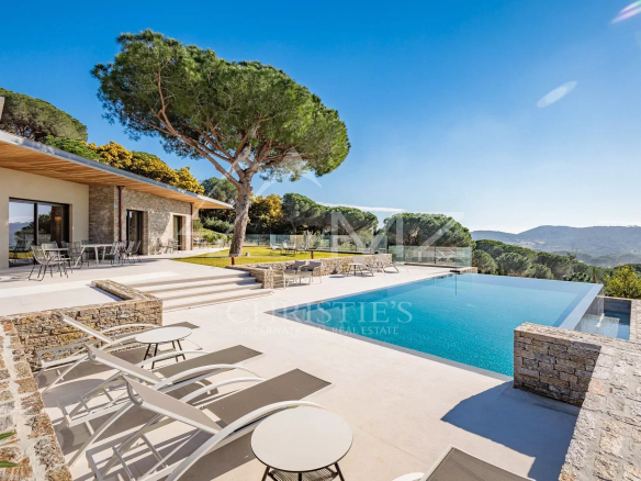 Vue de la piscine à débordement et de la terrasse d'une villa moderne à Ramatuelle, entourée de verdure.