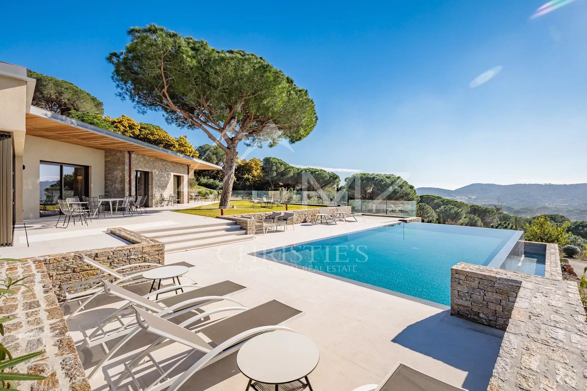Villa moderne avec piscine à Ramatuelle Vue de la piscine à débordement et de la terrasse d'une villa moderne à Ramatuelle, entourée de verdure.